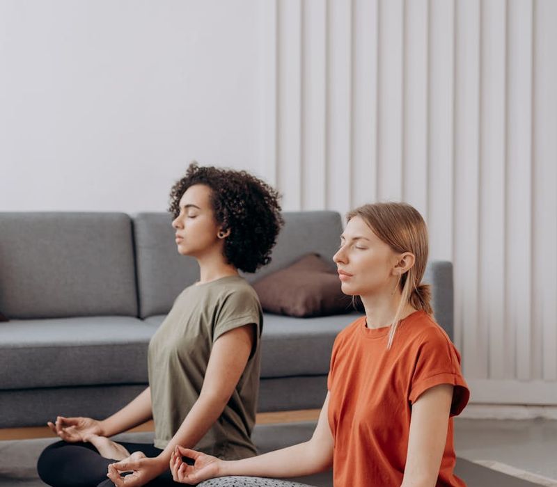 Person sitting in a calm meditation pose indoors in a bright room.